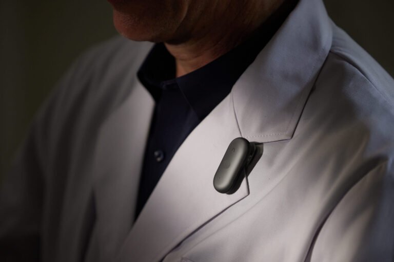 PLAUD NotePin S black recorder clipped to a jacket, showing its physical recording button